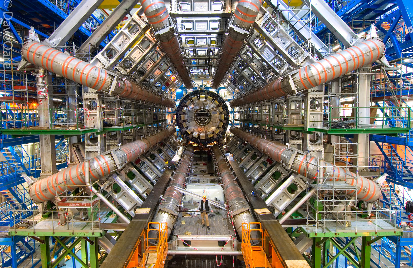 The enormous cylindrical ATLAS detector in its underground cavern, with a person standing at the center for scale.
