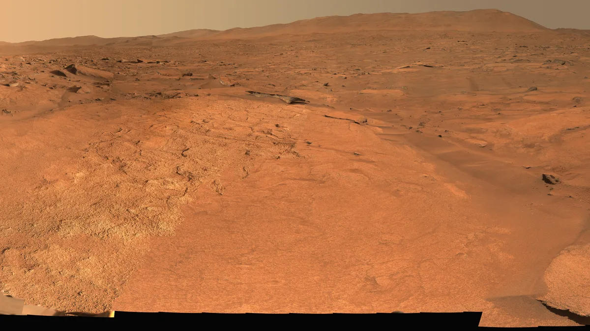 A rust-colored Martian plain and low hills under a pale sky, photographed by a rover.